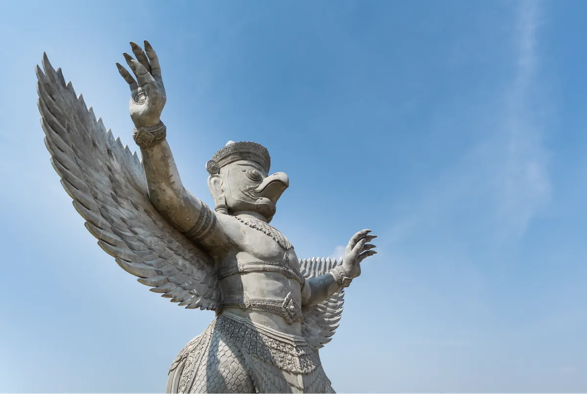 A stone statue of Garuda with raised wings, against the sky