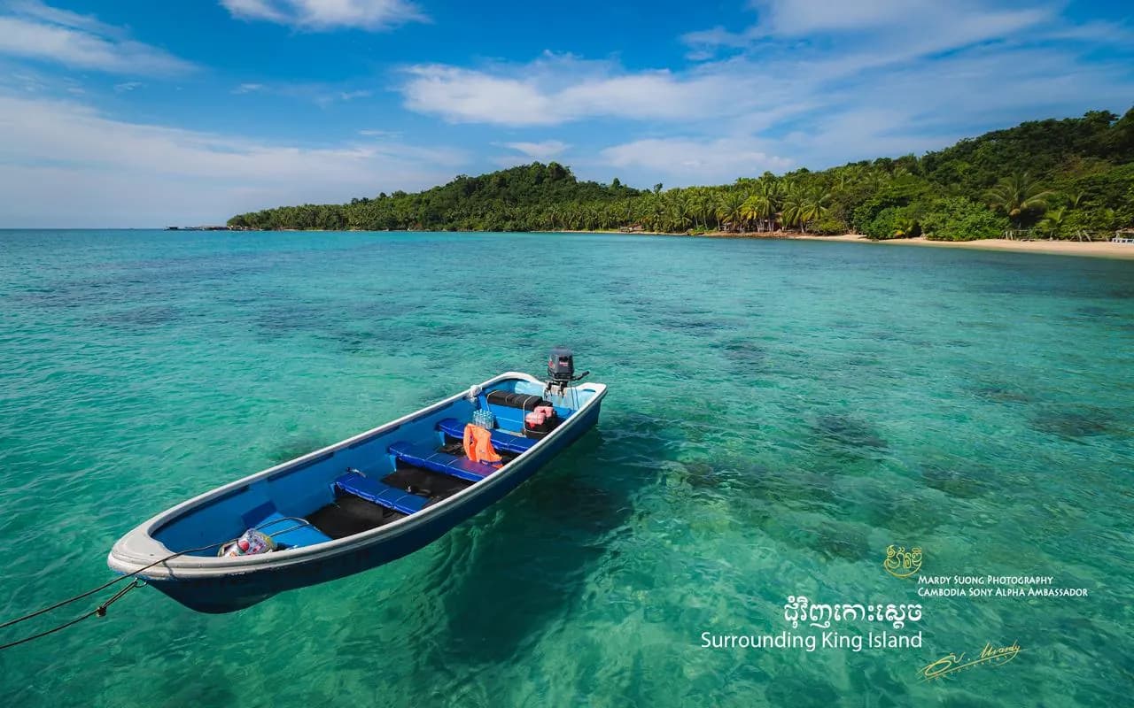 A small blue boat moored on clear turquoise water off a palm-lined island