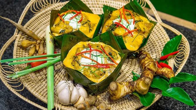 Amok in banana-leaf cups, on a woven tray with herbs and spices