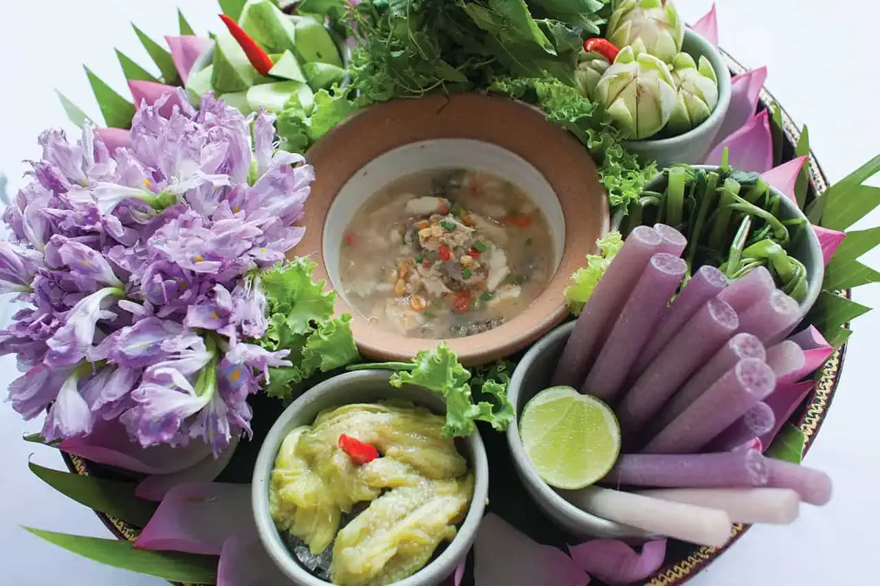 A dip surrounded by fresh vegetables and flowers