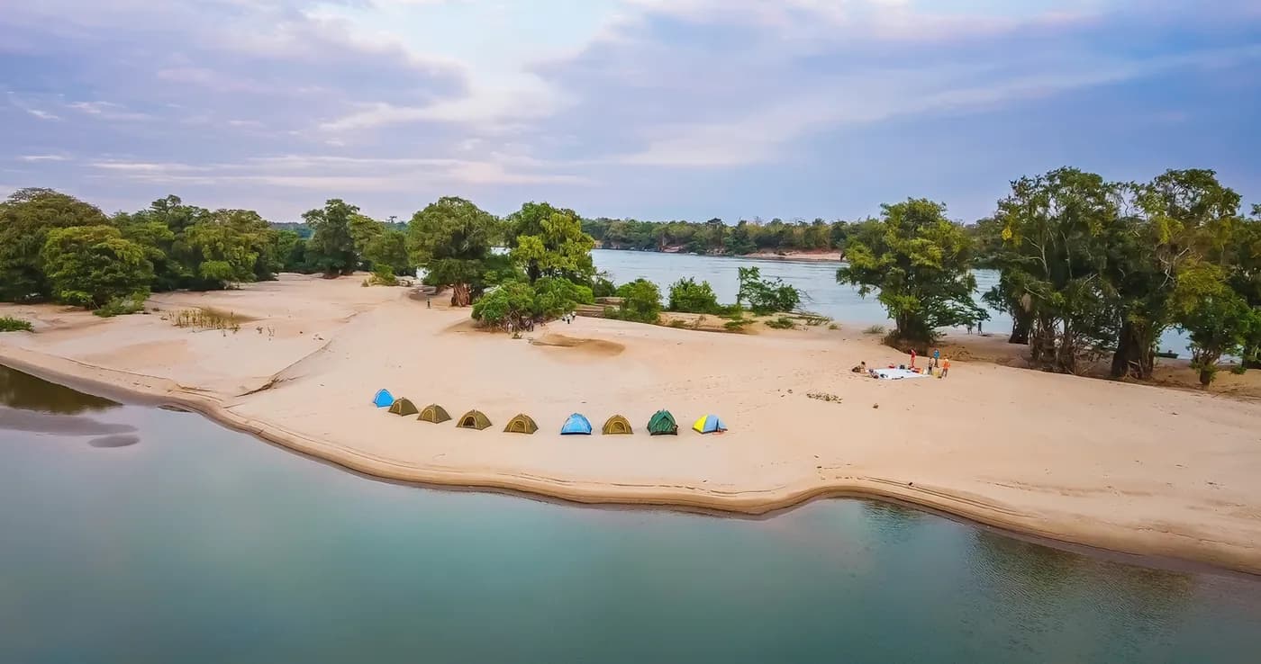 Tents on a sandy riverbank lined with trees