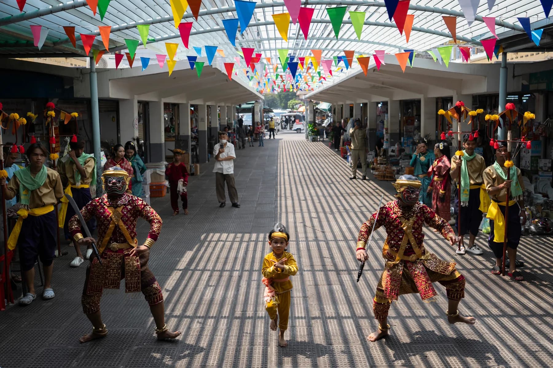 Robam Trot dancers at Phnom Penh’s Central Market: two masked performers and a child in gold, under strings of bunting