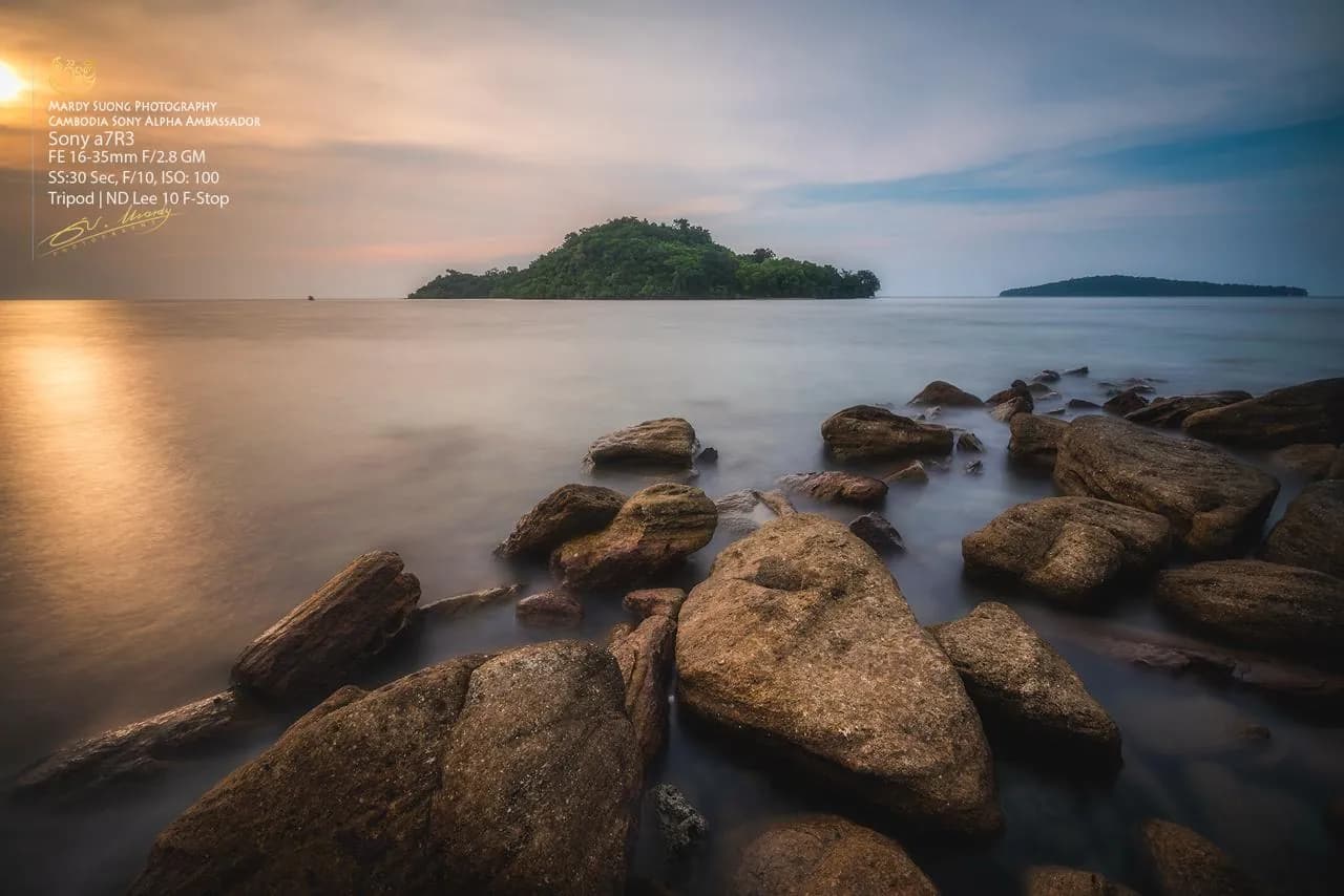 Smooth rocks in a calm sea at sunset, a small island on the horizon